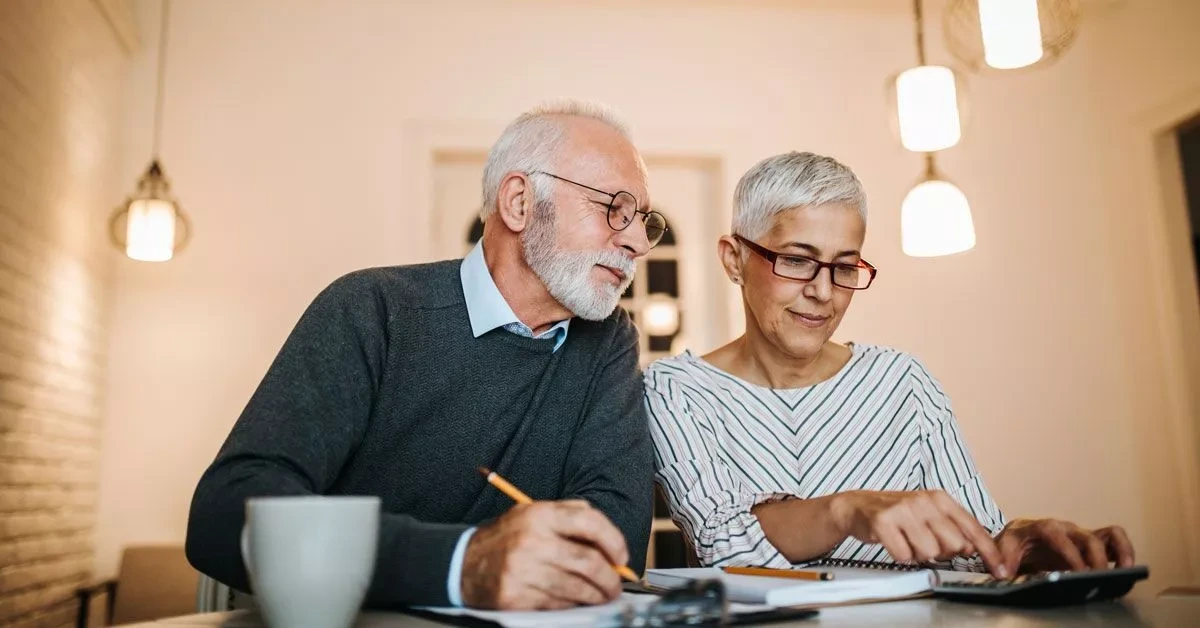 Retired couple at their kitchen table working through their finances with a notebook and calculator